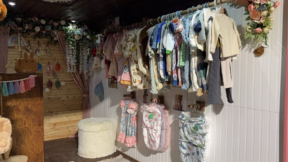 A rack of baby rompers, sleepers and swaddles hanging among silk florals in the studio.